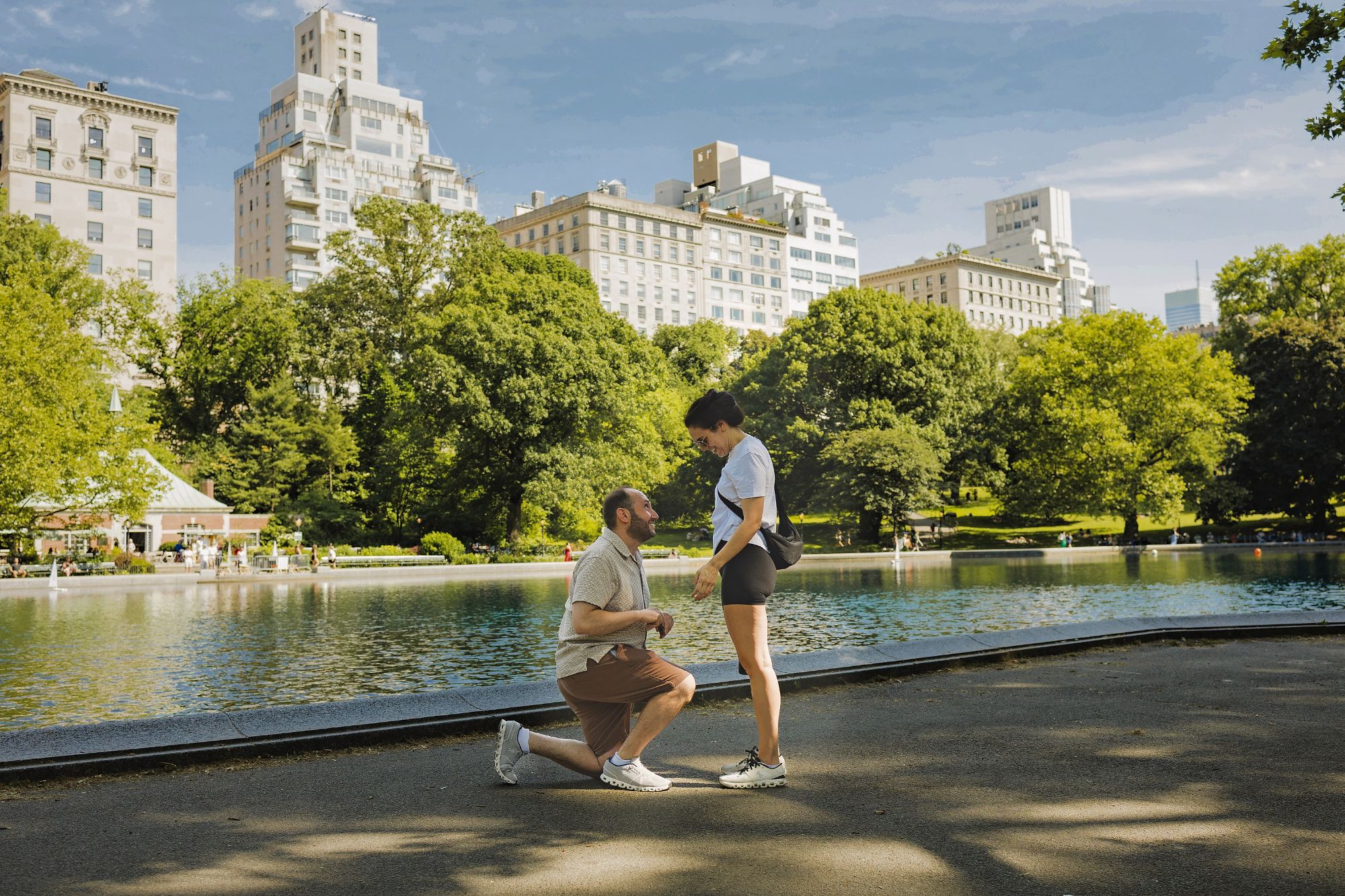 Pete kneeling to propose to Lisa beside the Conservatory Water in Central Park